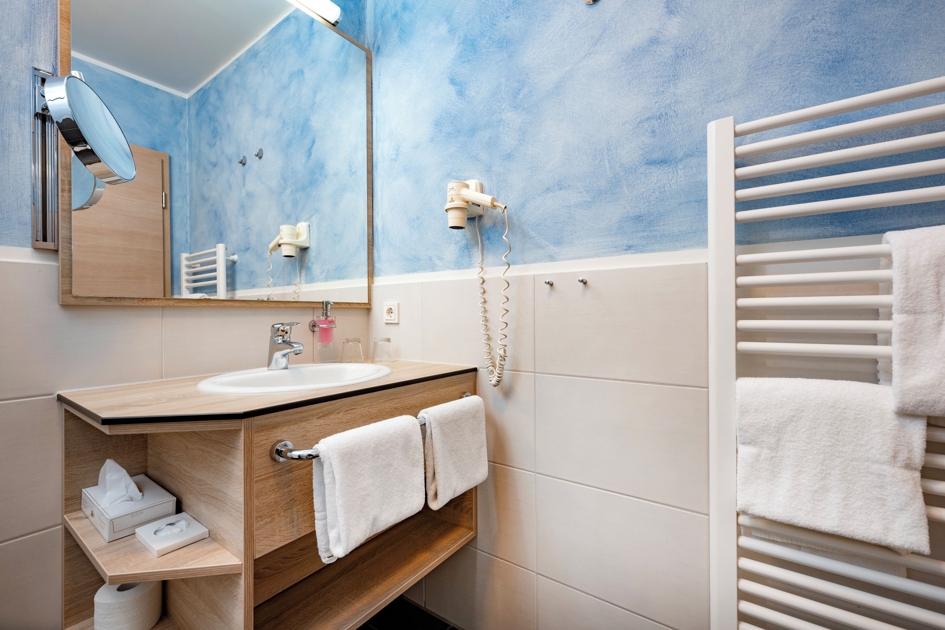 A bathroom with a wooden vanity, a mirror, a hairdryer, and a towel rack.