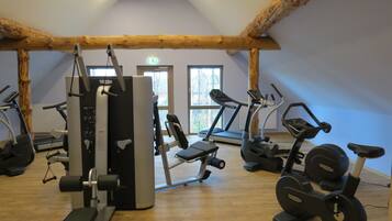 Un gimnasio con diverso equipo de ejercicios, incluyendo cintas de correr y máquinas de pesas, en un espacio con vigas de madera y ventanas amplias.