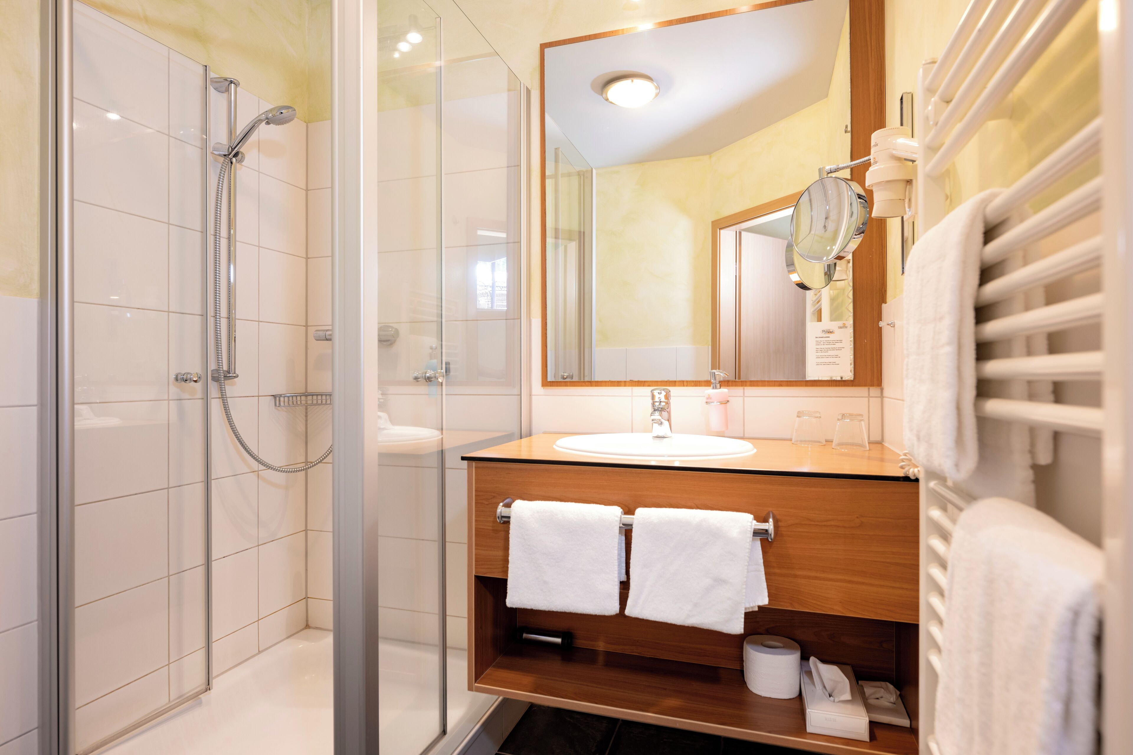 A modern bathroom with a glass-enclosed shower, a wooden vanity with a sink, and a large mirror.