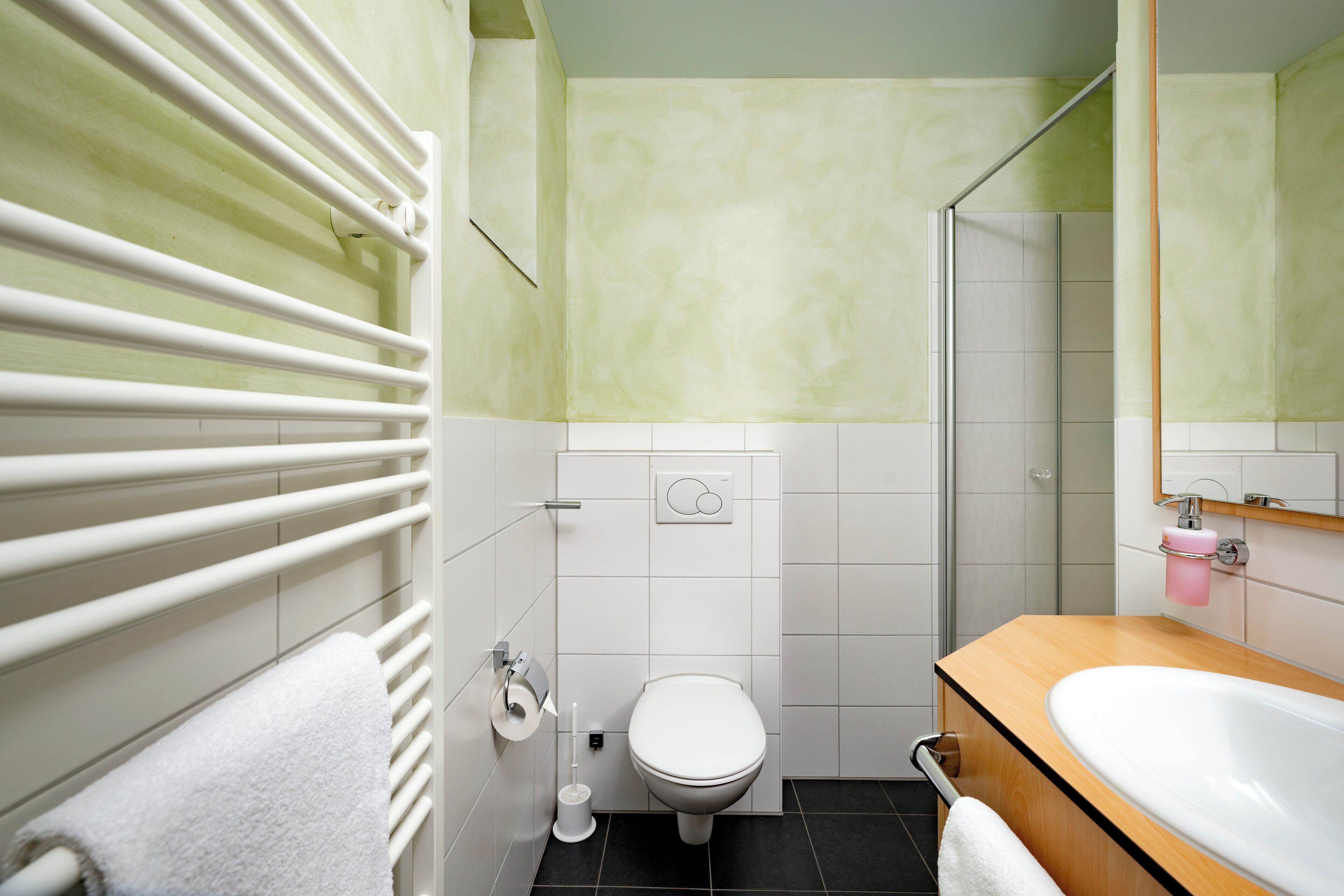 A bathroom with a white toilet, a shower, a sink, and a towel rack.