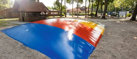 Une zone sablonneuse avec un tapis aux couleurs vives, une structure en bois et des arbres en arrière-plan.