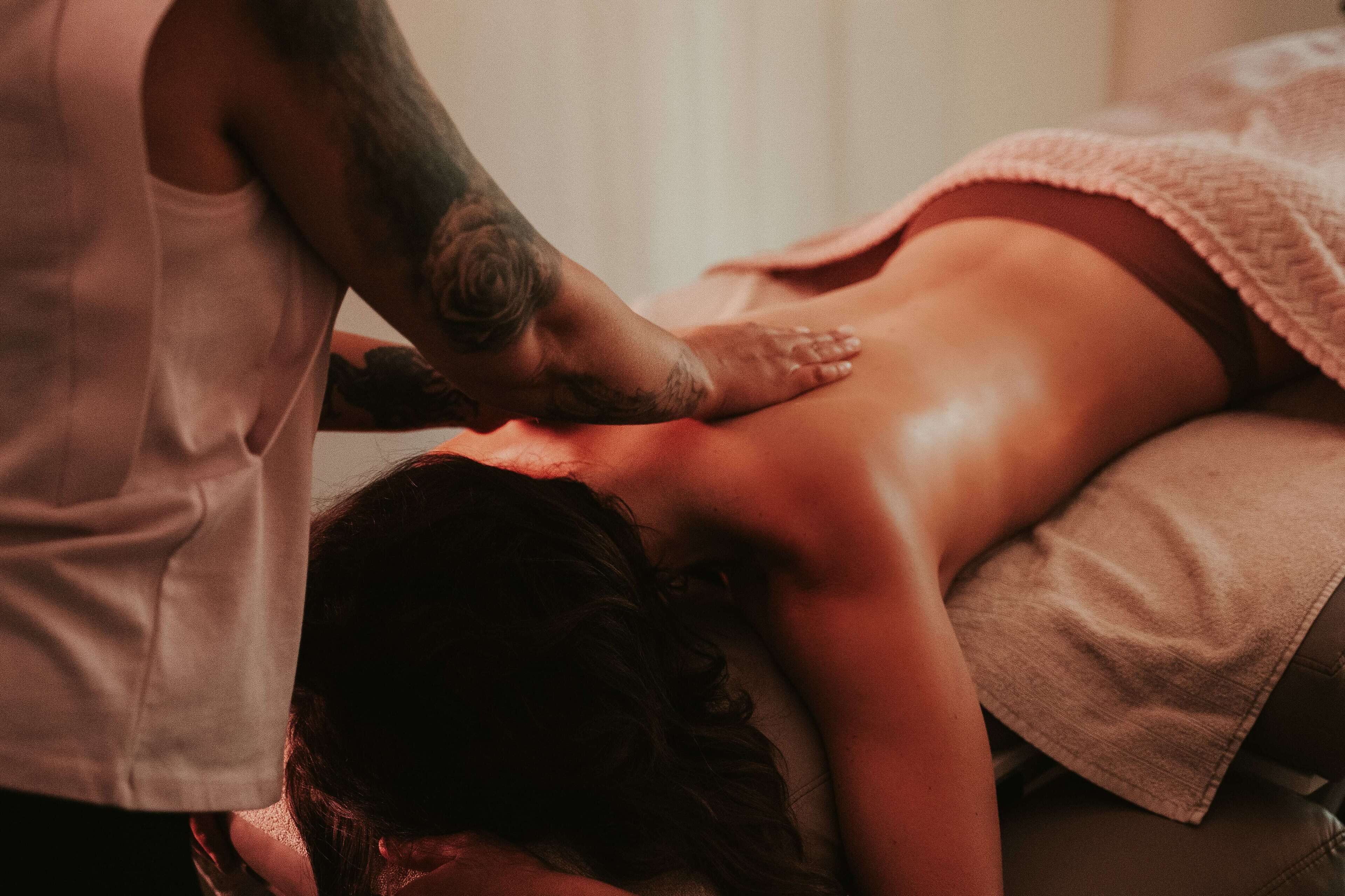 A person receiving a massage in a room with a bed and a blanket.