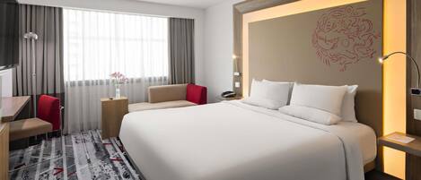 A hotel room with a large bed, a desk, a chair, and a TV.
