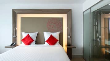 Une chambre d’hôtel moderne avec un grand lit, deux oreillers rouges, une table de chevet avec un téléphone et une cabine de douche en verre.