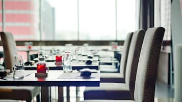 Un restaurante con mesas dispuestas para comer, sillas y vistas a edificios a través de grandes ventanales.