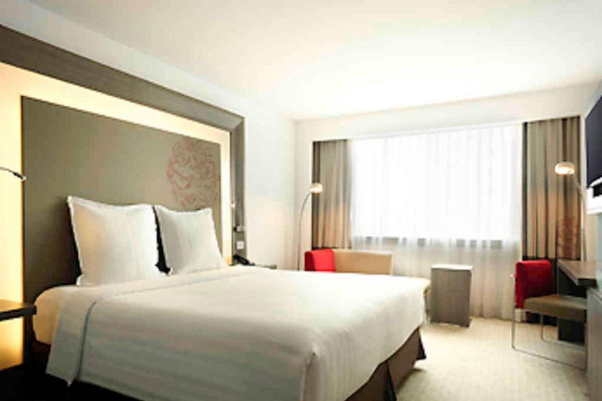 Ein Hotelzimmer mit einem großen Bett, einem Schreibtisch, einem Sessel, einem Fernseher und einem Fenster mit Vorhängen.