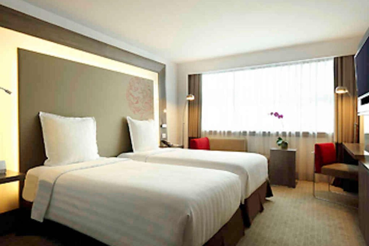 A hotel room with two beds, a desk, a chair, and a large window.