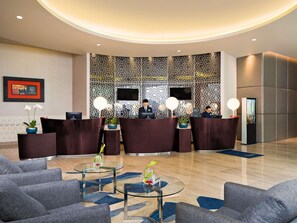 Een hotel lobby met een receptiebalie, een zithoek en decoratieve wandpanelen.