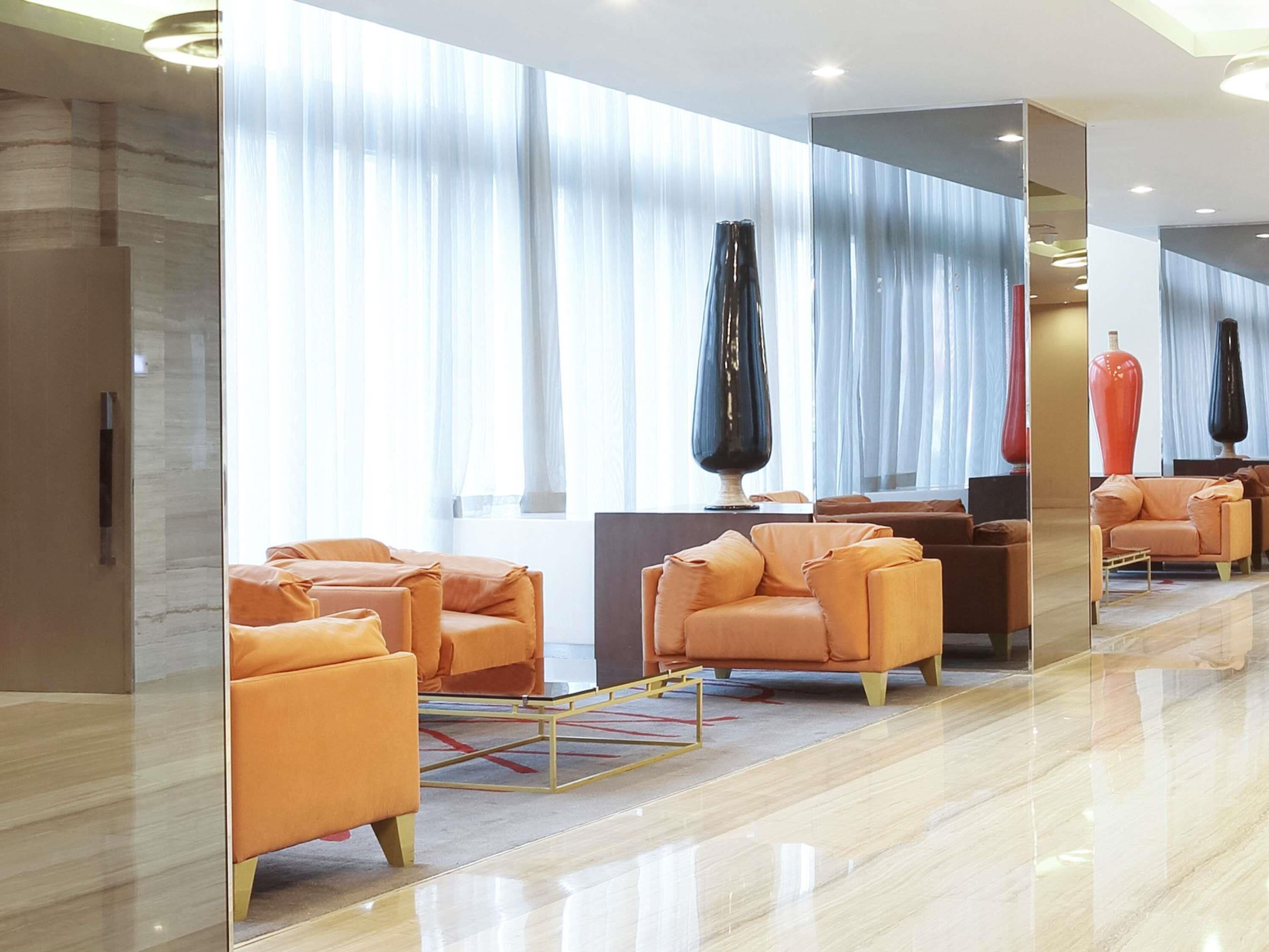 A modern hotel lobby with orange seating, large windows, and reflective surfaces.