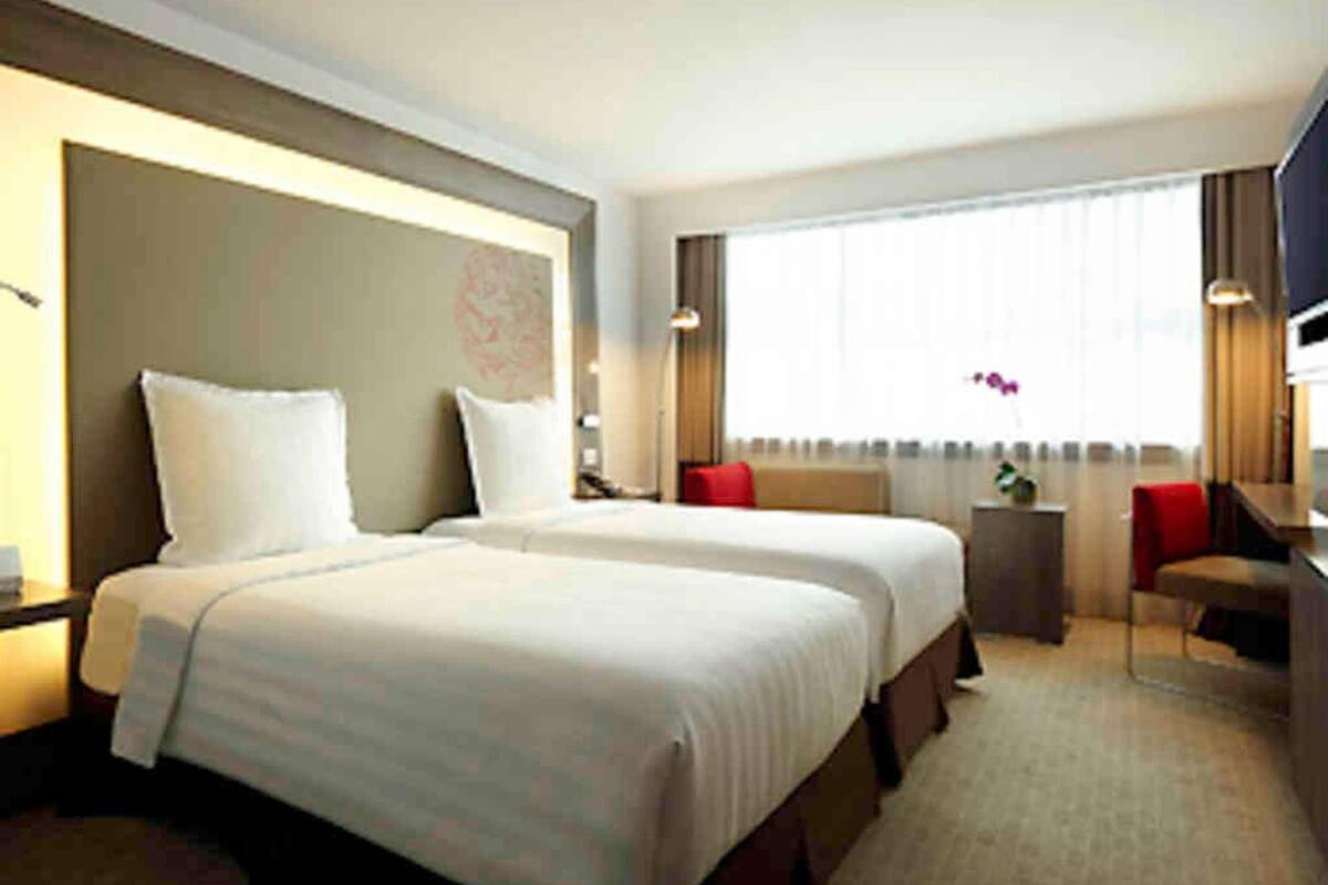 Ein Hotelzimmer mit zwei Betten, einem Schreibtisch, einem Stuhl und einem großen Fenster.