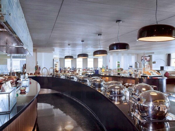 Un moderno vestíbulo de hotel con un mostrador de recepción curvo, zona de buffet e imponentes lámparas colgantes.