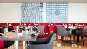 A restaurant with tables set for dining, red cushioned seating, and a patterned wall in the background.