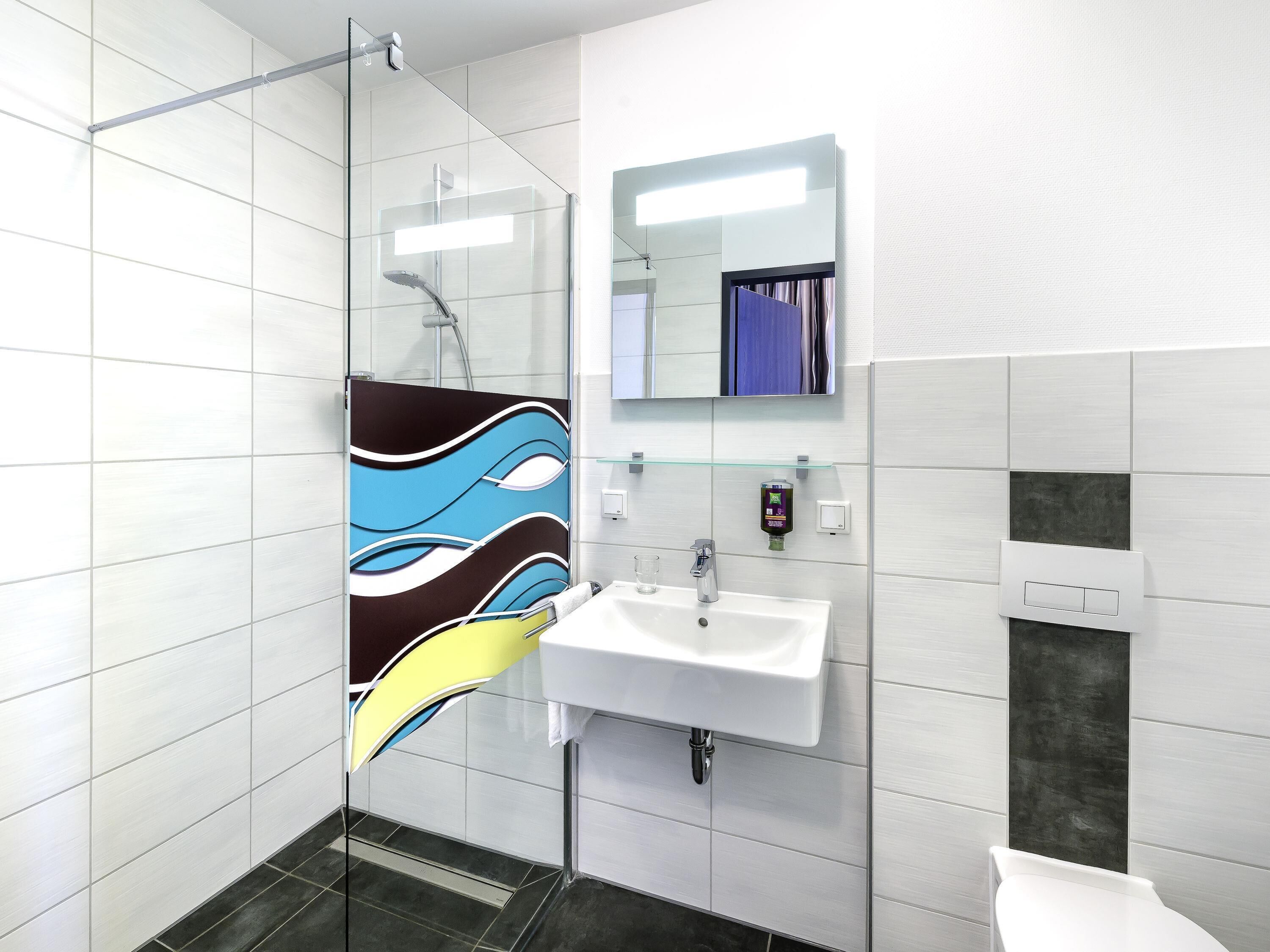 Un baño moderno con cabina de ducha de vidrio, un lavamanos blanco y un espejo encima.
