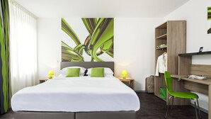 A modern hotel room with a large bed, two bedside tables with lamps, a desk with a chair, and a wardrobe.