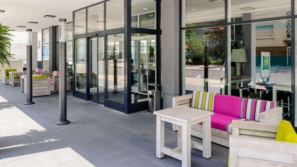 An outdoor seating area with tables and chairs, a glass entrance, and a view of the street.