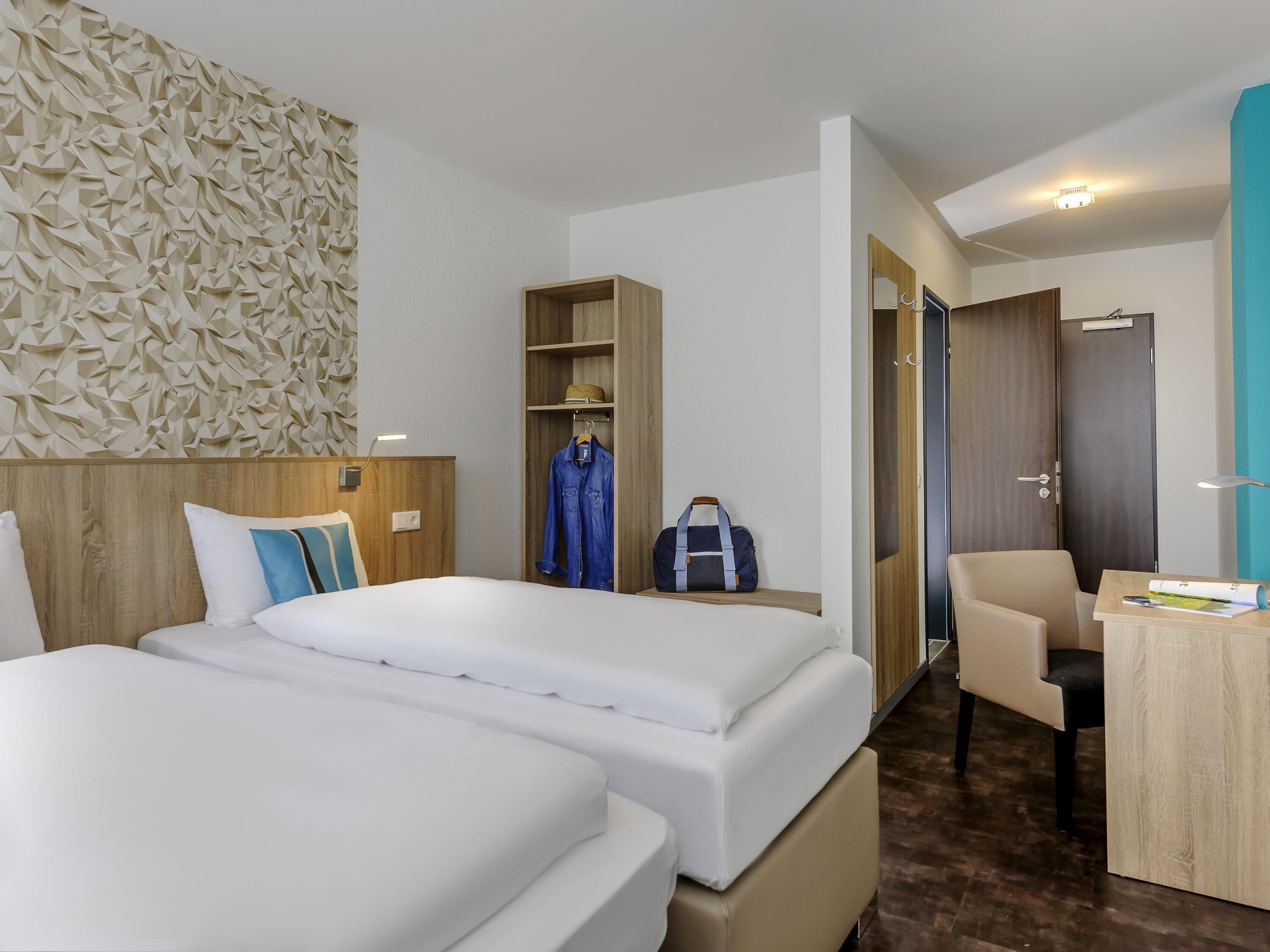 A hotel room with two beds, a wardrobe, a desk, and a chair.