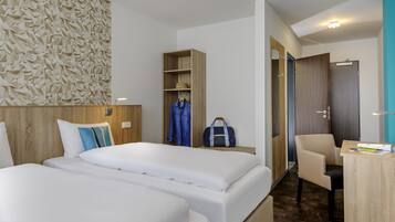 A hotel room with two beds, a wardrobe, a desk, and a chair.