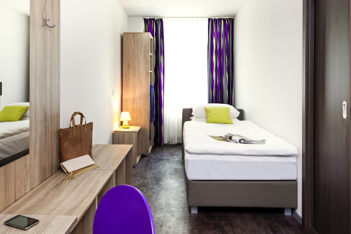 Una camera d'albergo con un letto, una scrivania, una sedia, un armadio e l'ingresso del bagno.