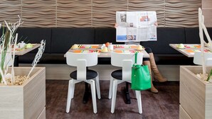 A modern restaurant with a wavy wall design, tables with colorful placemats, and a person reading a newspaper.