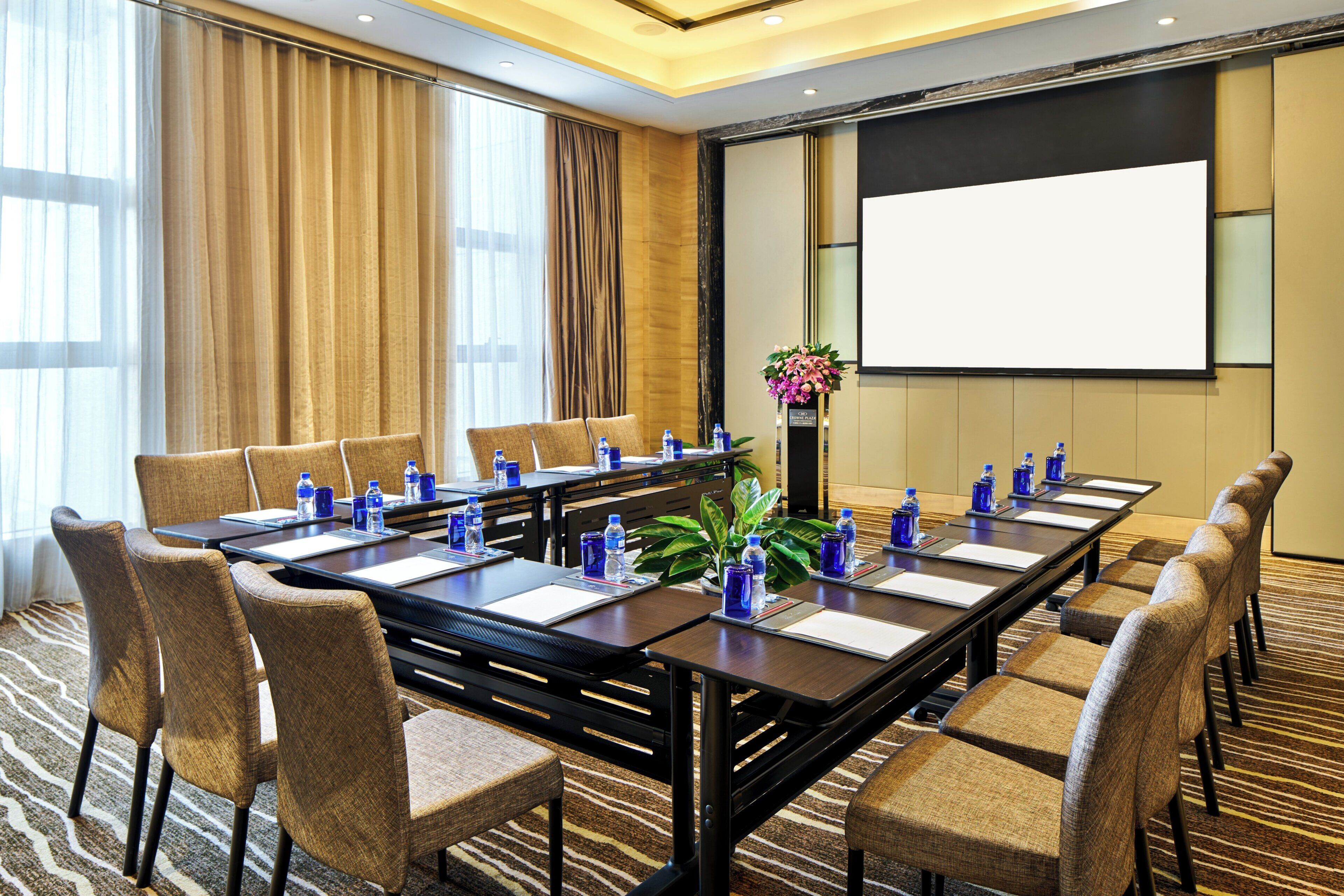 A conference room with a long table, chairs, water bottles, and a projector screen.