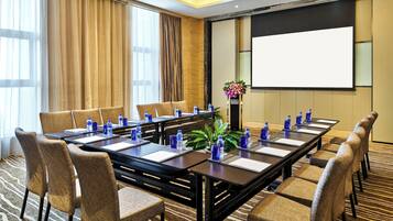 A conference room with a long table, chairs, water bottles, and a projector screen.