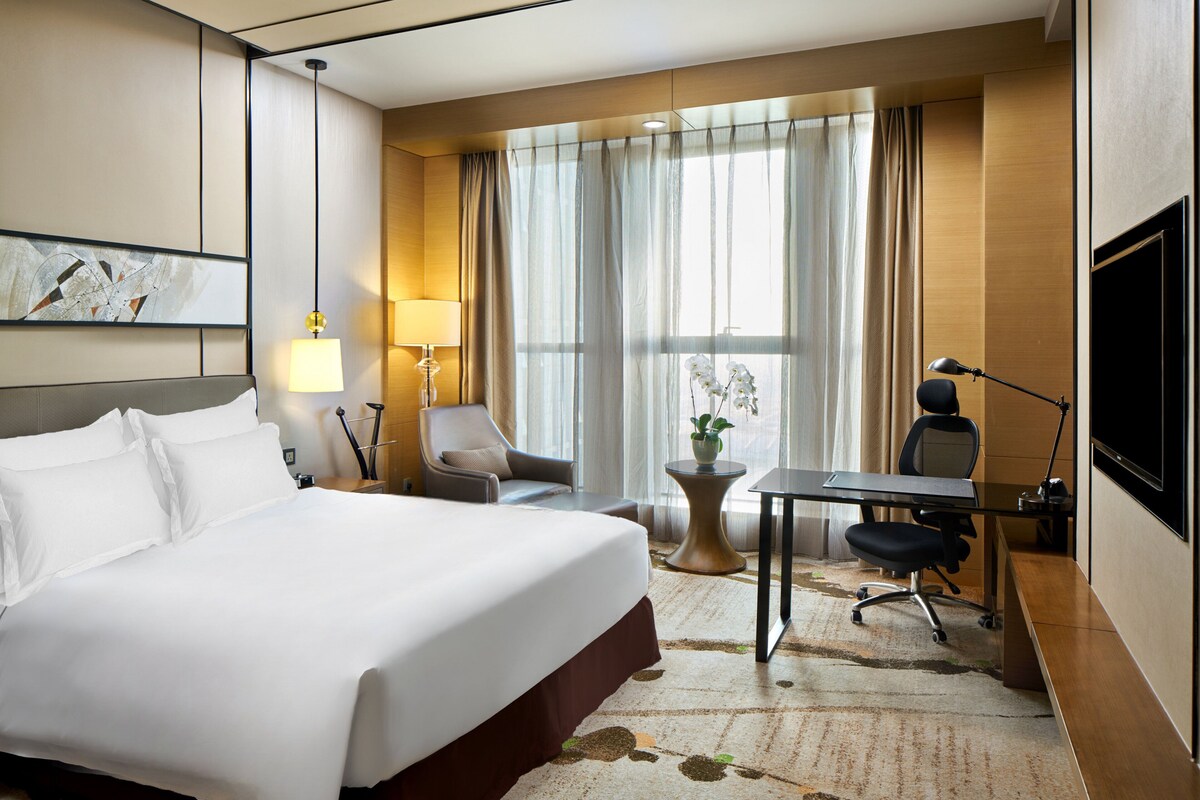 Una habitación de hotel con una cama grande, un escritorio, una silla, un televisor y una ventana con cortinas.