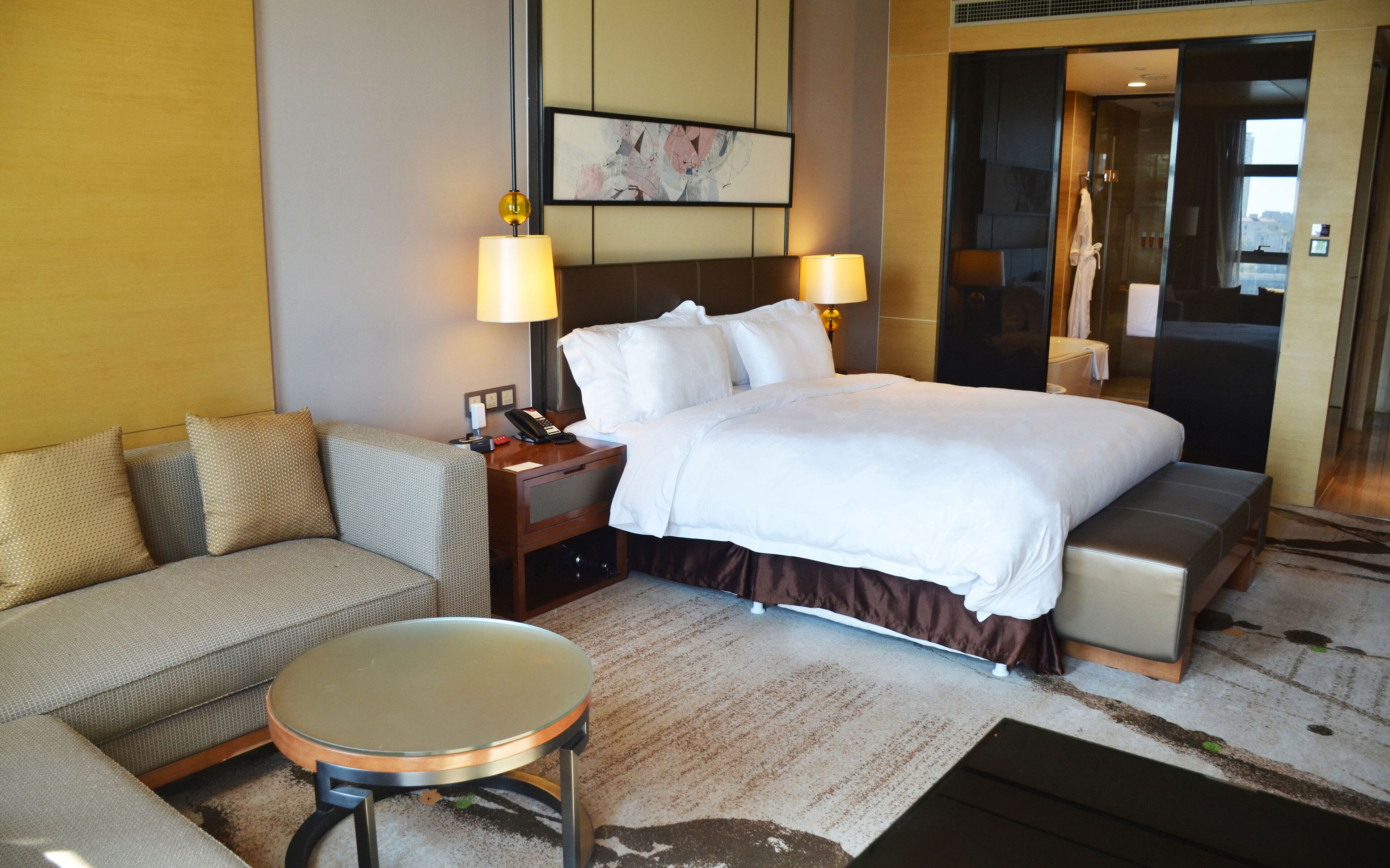 Una habitación de hotel con cama, sofá, una mesita y un baño visible a través de una puerta abierta.