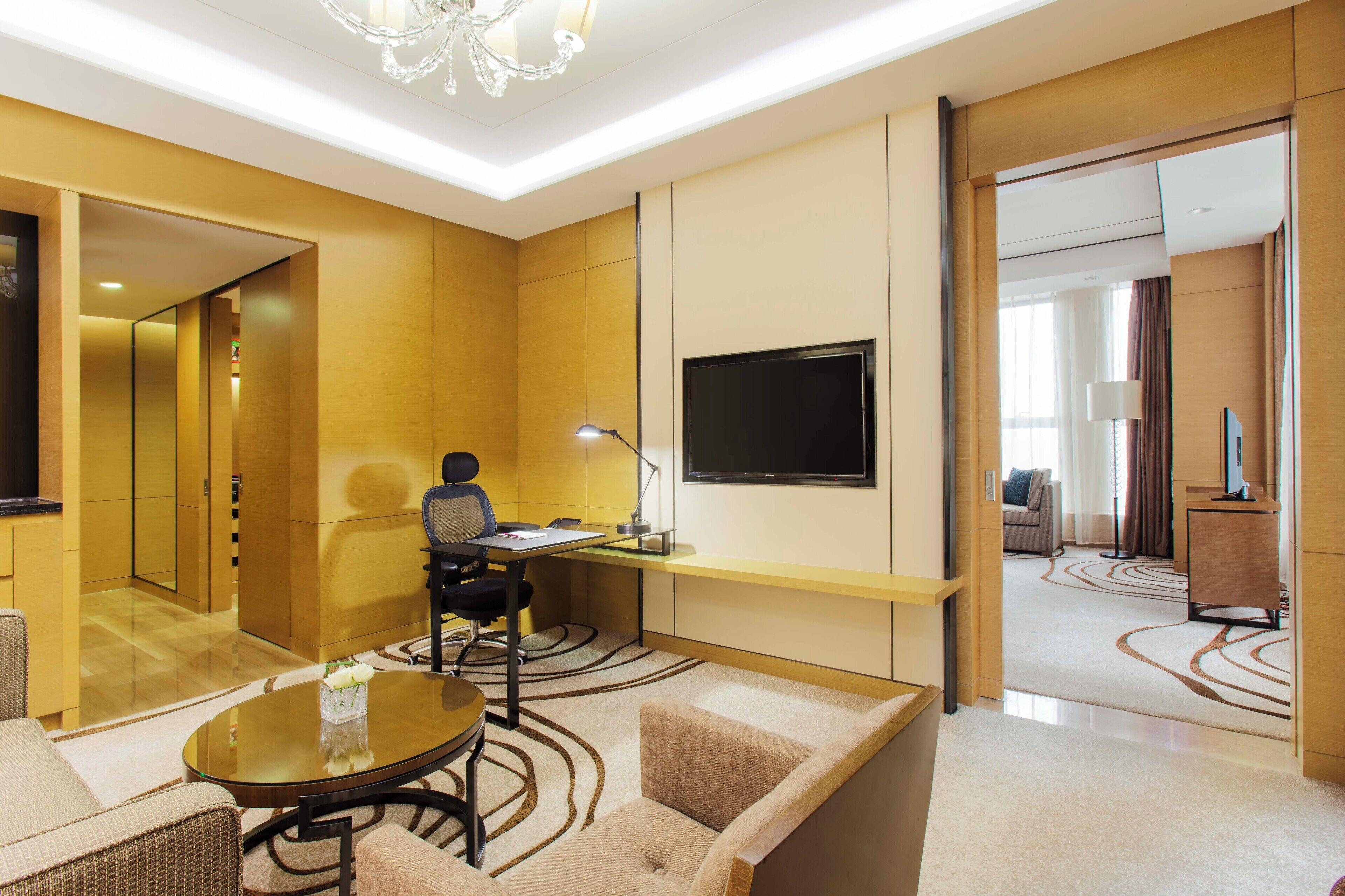 A hotel room with a desk, chair, sofa, and a TV.