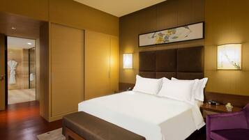 A hotel room with a large bed, a wooden headboard, a bedside table with a lamp, and a purple chair.