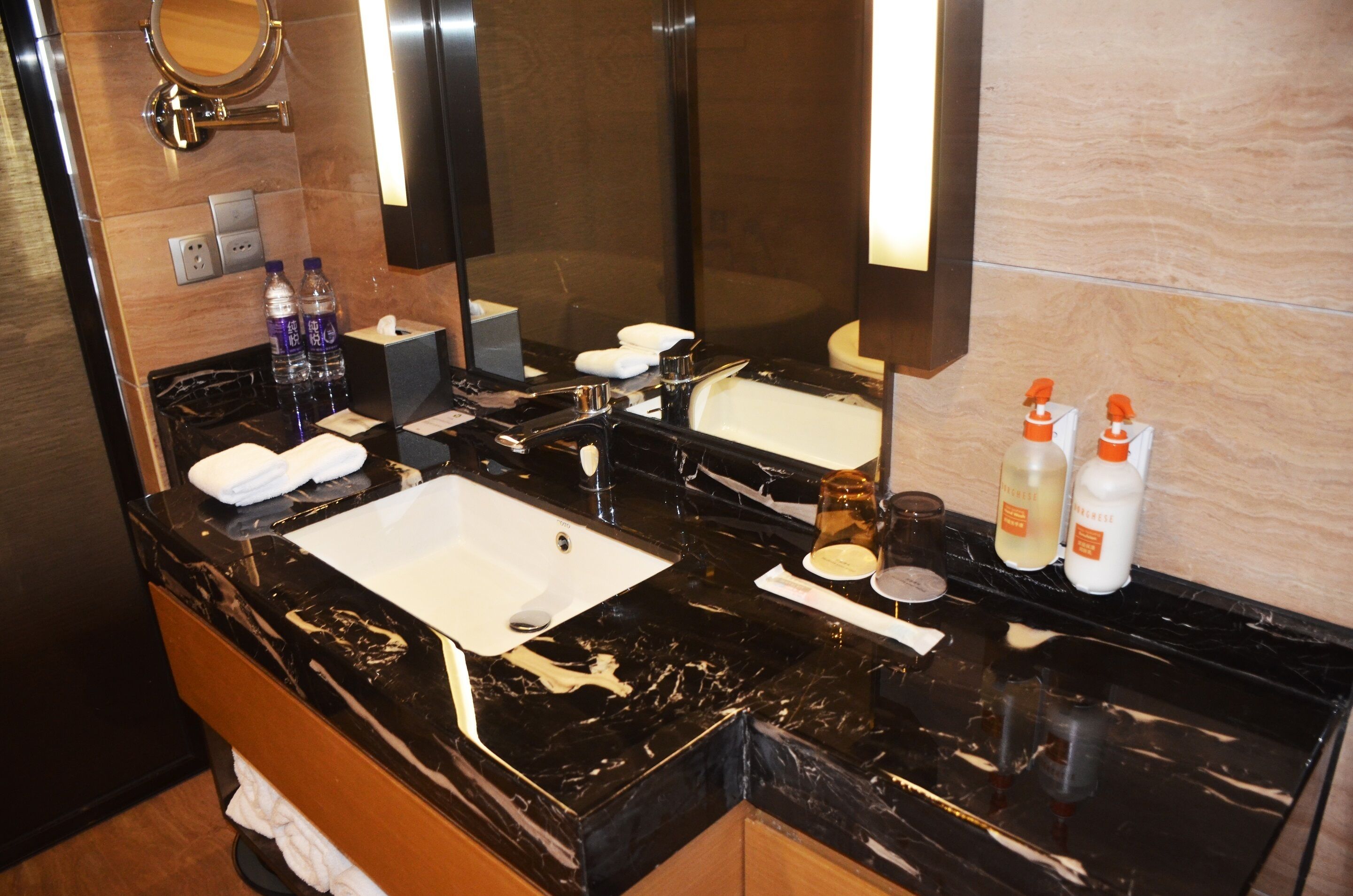 A modern bathroom with a black marble sink, two mirrors, and toiletries on the counter.