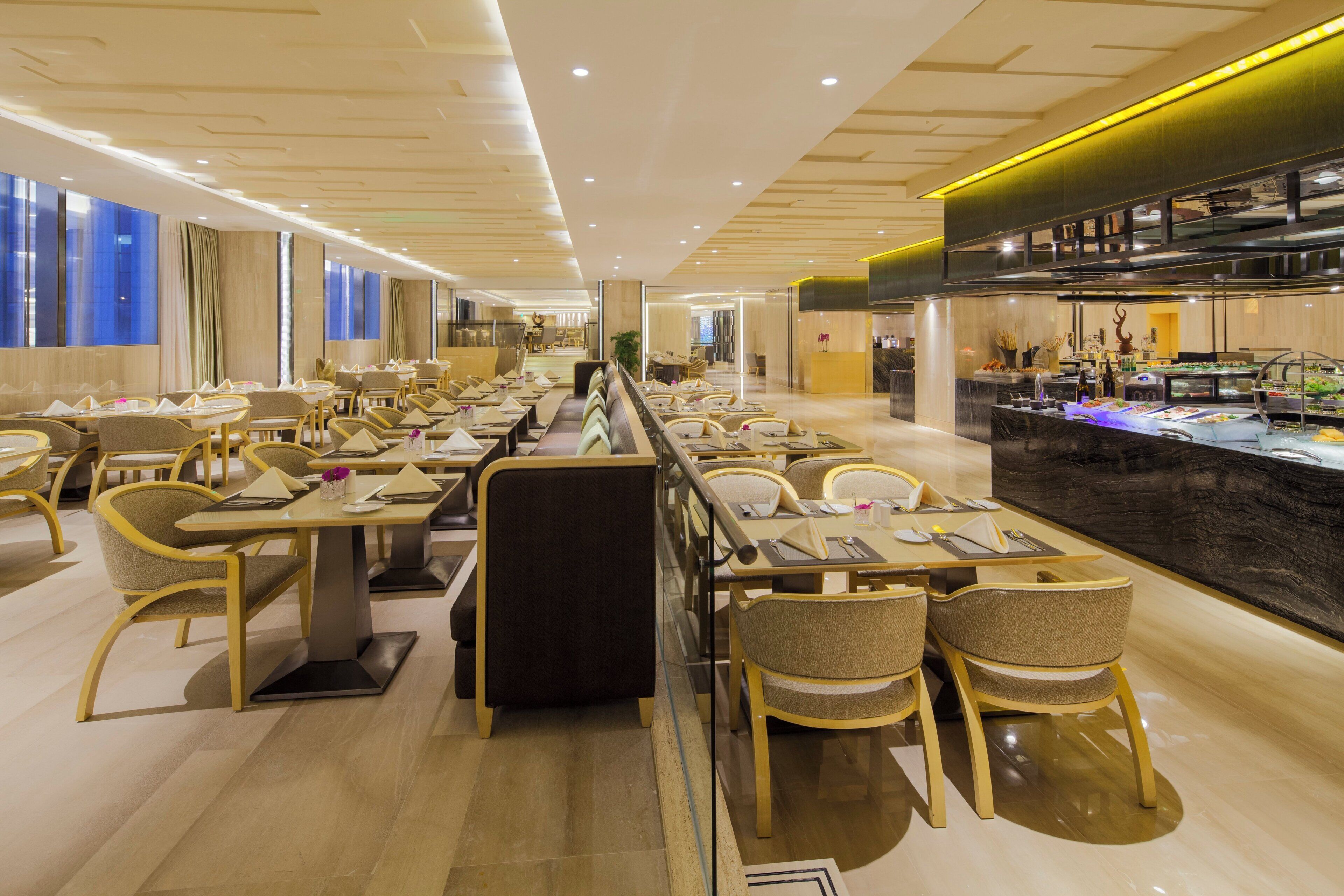 Un restaurant modern amb taules comunitàries llargues i seients individuals, una zona de bar i vista a la ciutat a través de grans finestres.