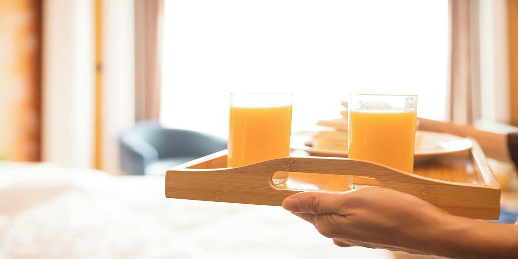Una bandeja de madera con dos vasos de jugo de naranja sostenida por una persona.