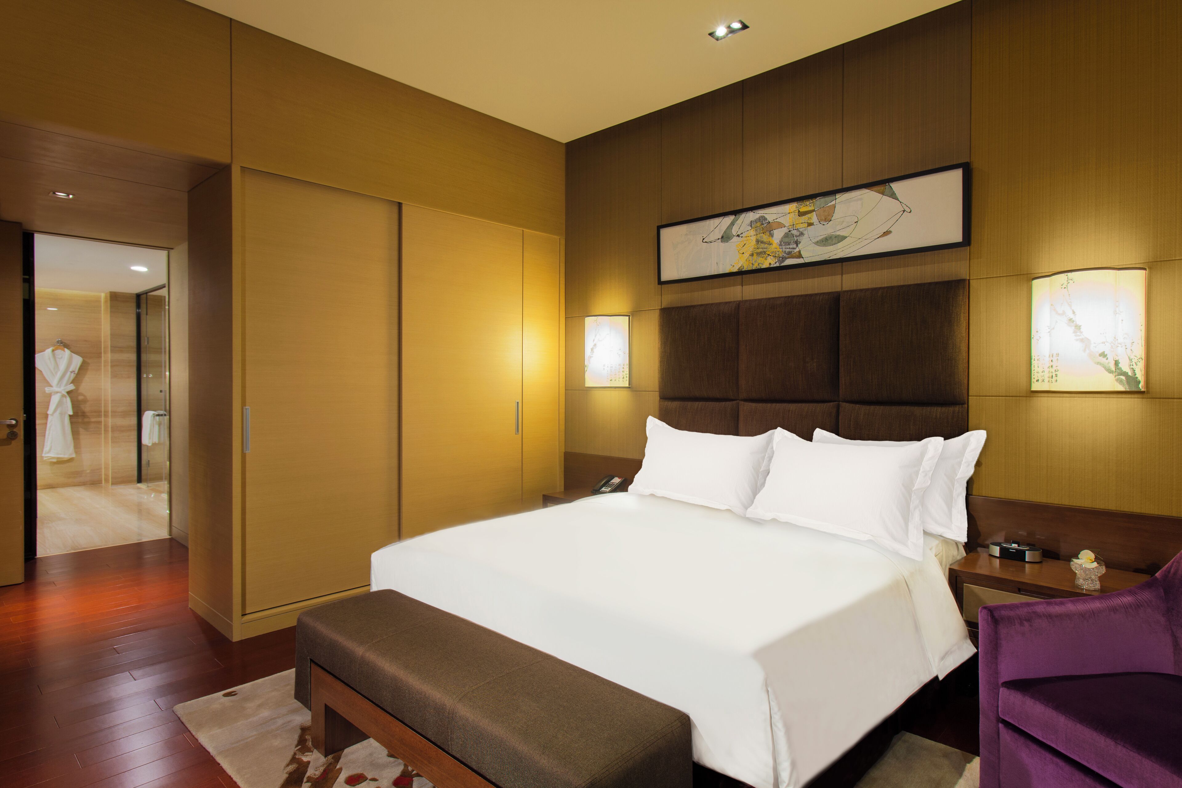 Una habitación de hotel con una cama grande, cabecera de madera, una mesita de noche y una silla morada.