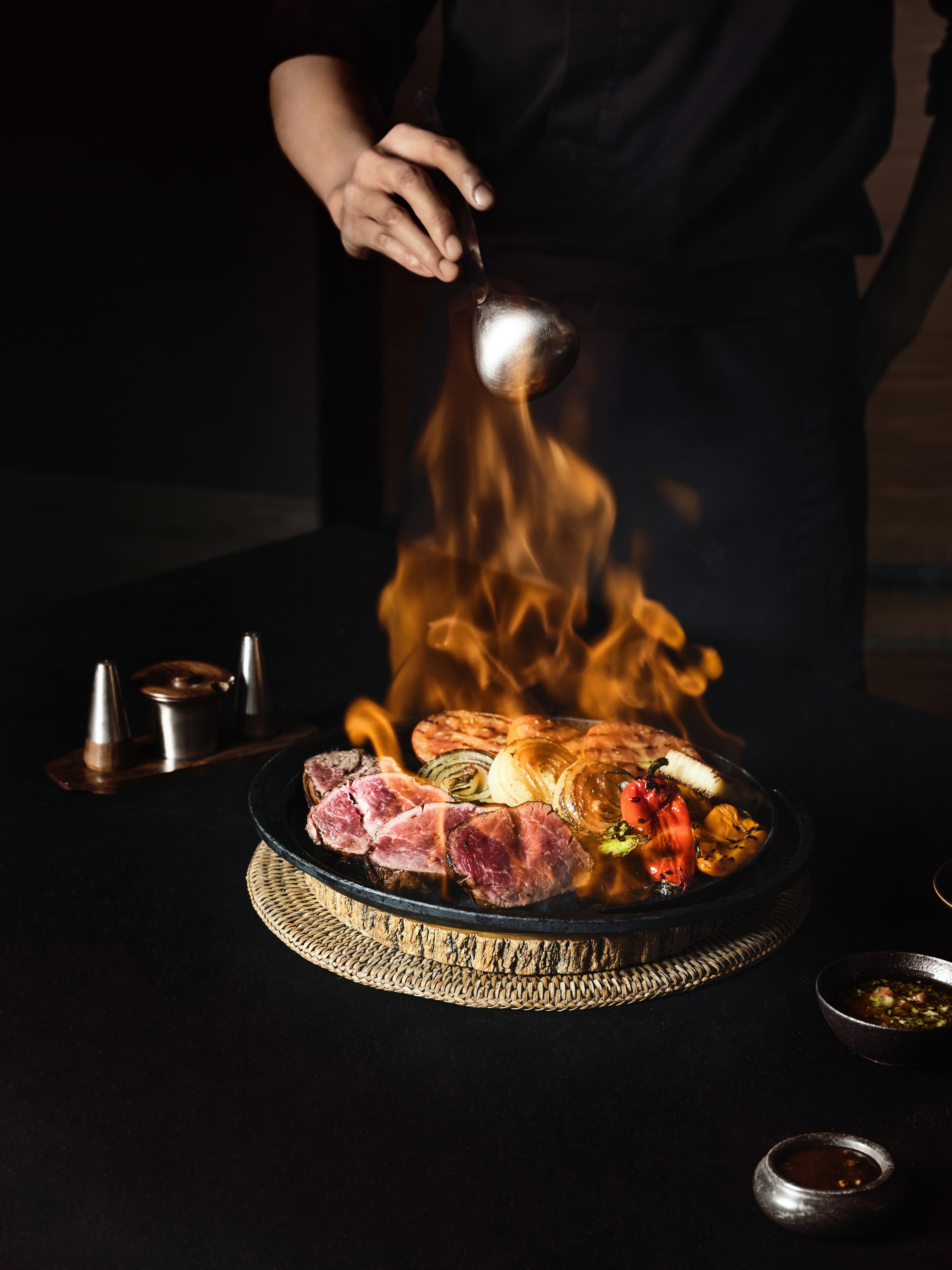 A chef cooking meat over an open flame on a grill.