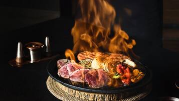 A chef cooking meat over an open flame on a grill.