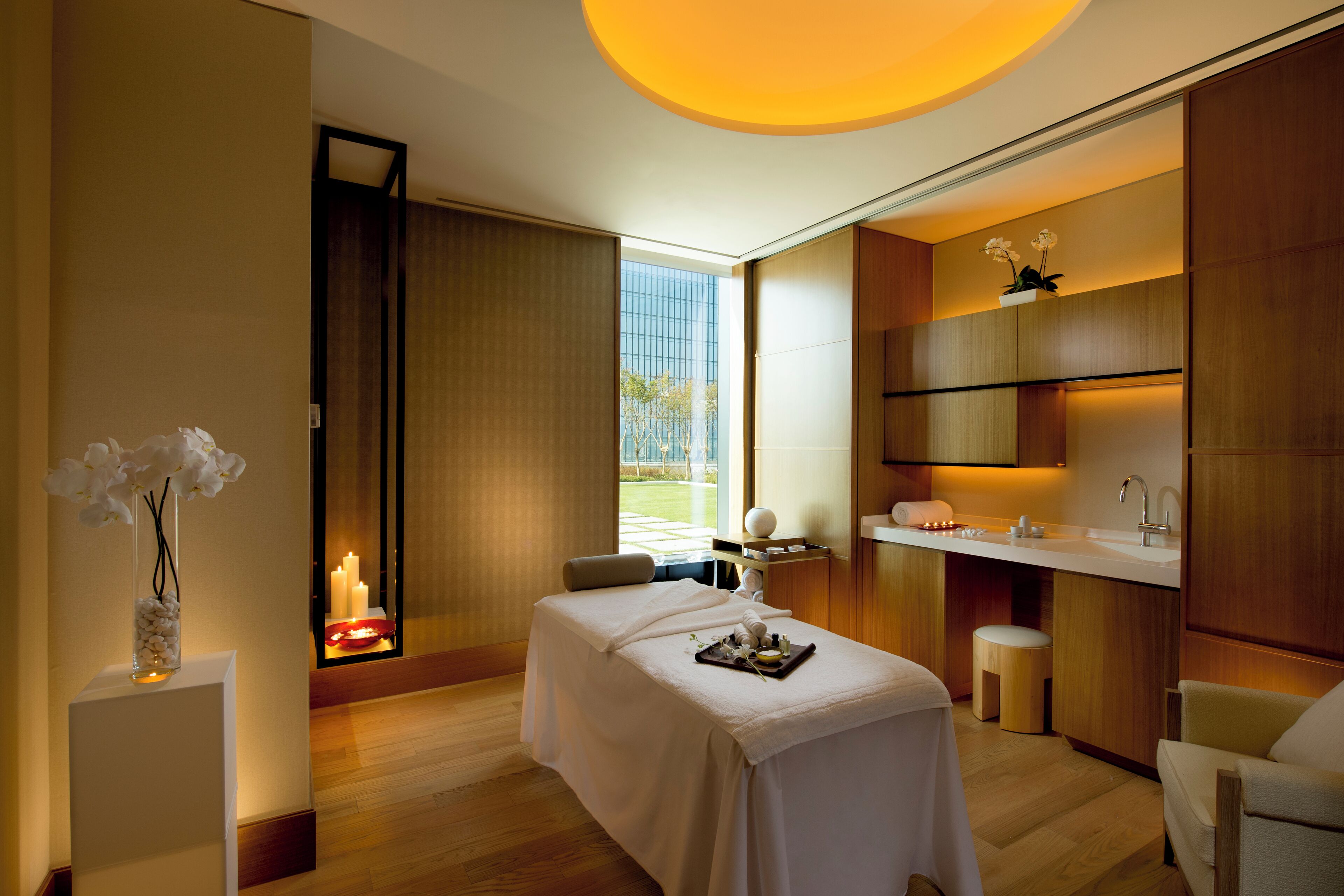 A modern spa room with a massage table, a small stool, and a reception desk.