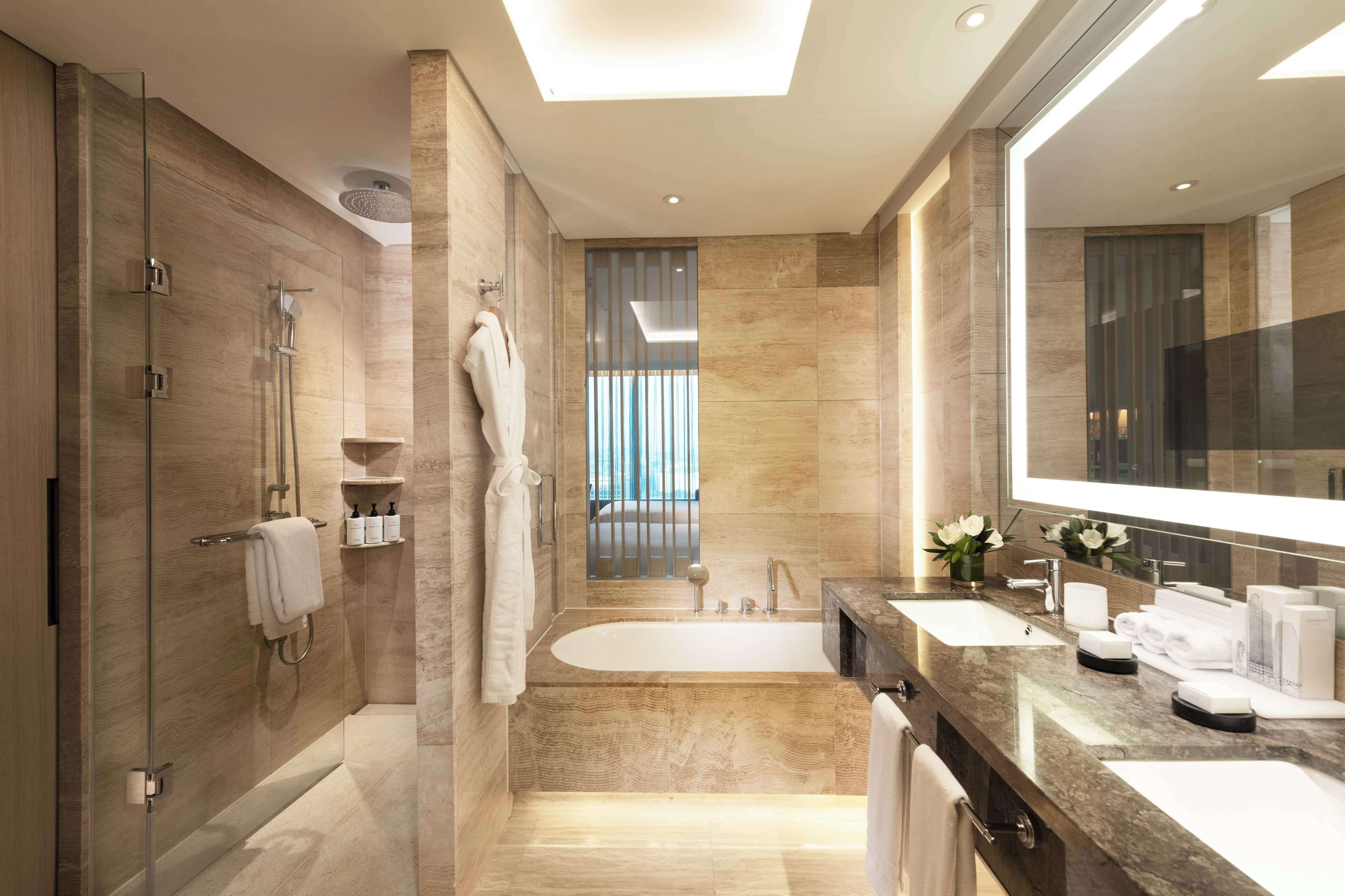 Un baño moderno con ducha envuelta en vidrio, una bañera independiente y un mueble de tocador espacioso con lavamanos dobles y un espejo.