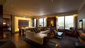 A modern hotel room with a large bed, a sitting area with a sofa and armchairs, a dining table, and a city view through large windows. - Conrad Seoul (Seoul)