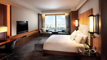 A hotel room with a large bed, a TV, a desk, and a view of the city.