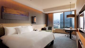A modern hotel room with a large bed, a desk, and a view of the cityscape.