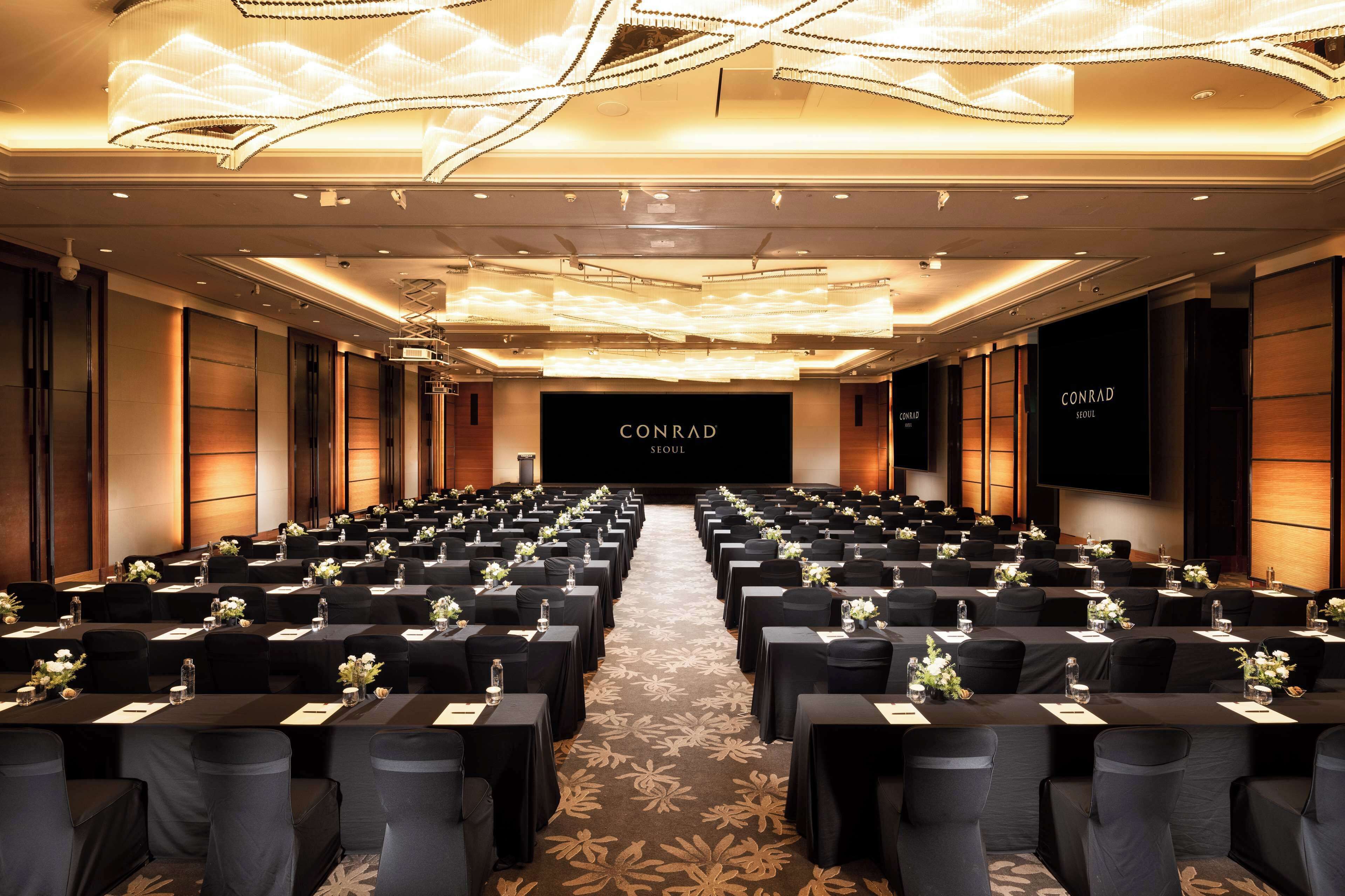 A conference room with rows of tables, black tablecloths, and floral centerpieces.