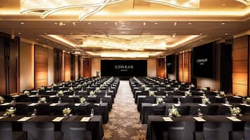 A conference room with rows of tables, black tablecloths, and floral centerpieces.