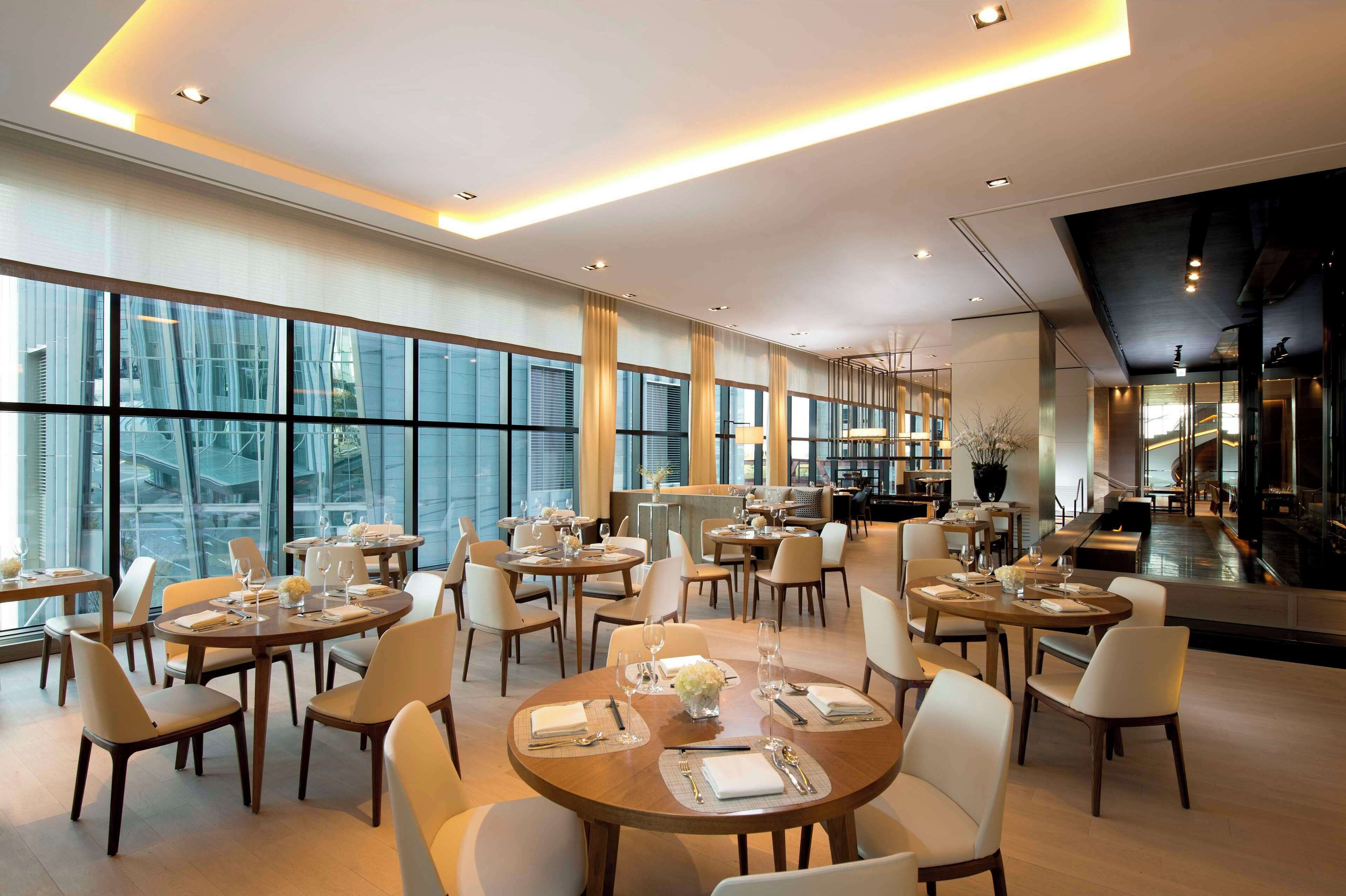 Uma sala de jantar ampla com várias mesas redondas, cadeiras e um espaço de bar.