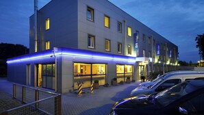 Ein modernes Hotel mit flacher Fassade, zahlreichen Fenstern und einem überdachten Außenbereich mit blauer Neonlichtleiste.