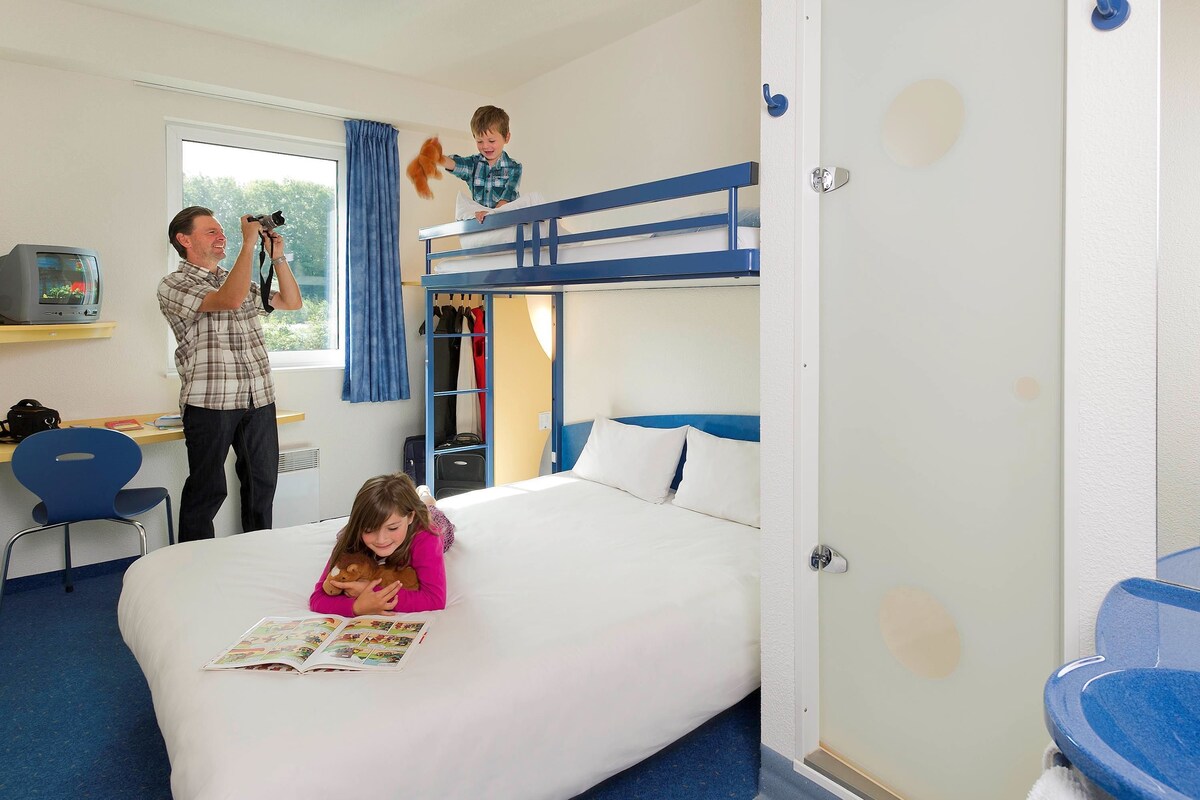 A hotel room with a bunk bed, a desk with a television, and a chair.