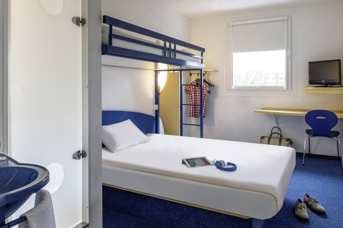 Hotelkamer met een stapelbed, een bureau met een computer, een stoel, een televisie en een paar schoenen op de vloer.