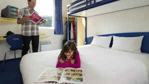 Ein Hotelzimmer mit einem Etagenbett, einem Schreibtisch inklusive Computer und einem Fenster mit Vorhängen.