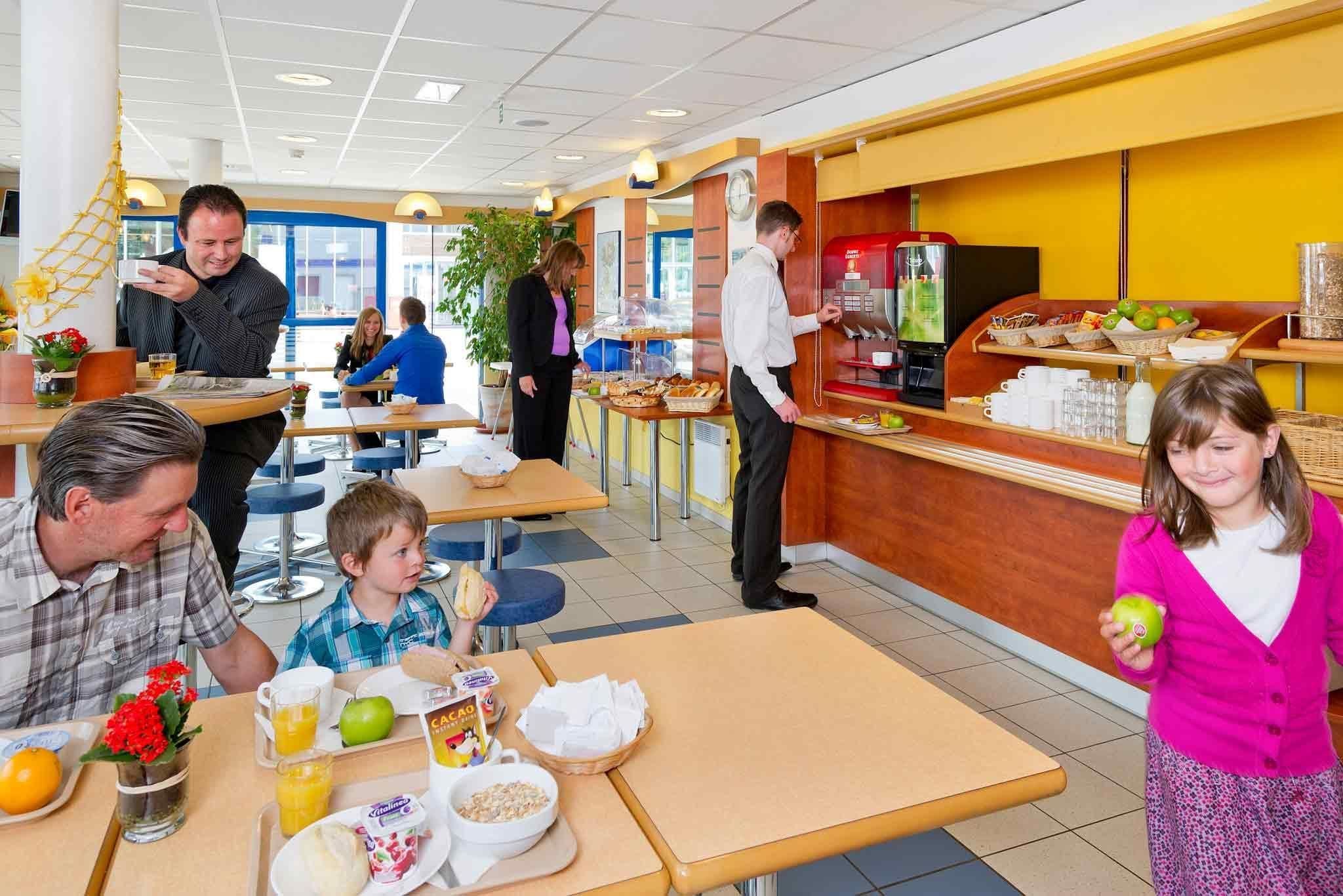 A breakfast area with tables, a coffee station, and a buffet with fruits and pastries.