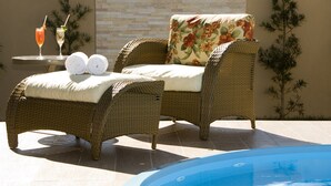 A wicker lounge chair with a floral cushion, a small table with drinks, and a pool in the foreground. - BH Jaraguá Hotel (Belo Horizonte)