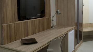 A modern office space with a built-in TV, desk, chair, and a small refrigerator.